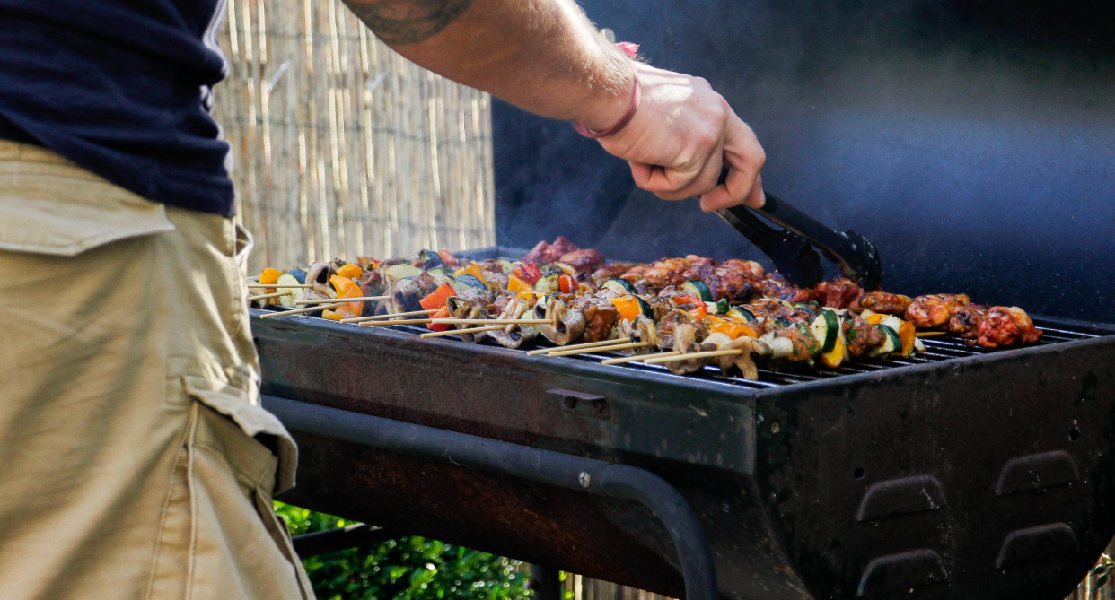 BBQ, man with tattoo on arm wearing beige cargo shorts standing next to bbw with food on grill