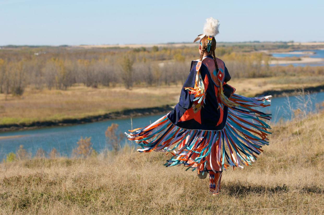 First Nations Women performing a Fancy Shawl Dance in a grass field with a river background