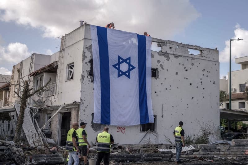 People hang a giant Israeli flag from the roof of a damaged building in Kiryat Bialik, following a reported strike by the pro-Iranian Hezbollah movement. Ilia Yefimovich/dpa