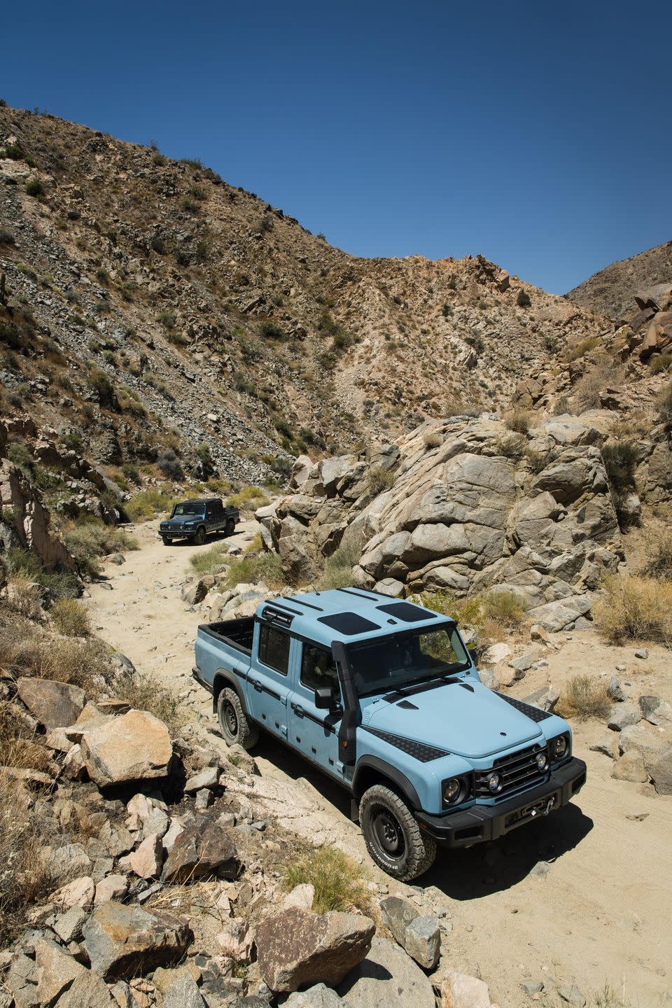 a blue ineos grenadier driving on a rocky hill