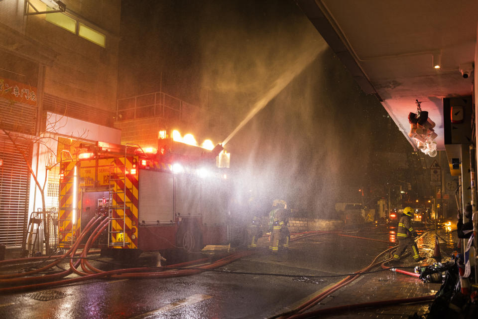 Firefighters battle a fire as debris falls from the building in Hong Kong, Friday, March 3, 2023. Hong Kong firefighters are battling the blaze that broke out at a construction site in the city's popular shopping district. (AP Photo/Louise Delmotte)