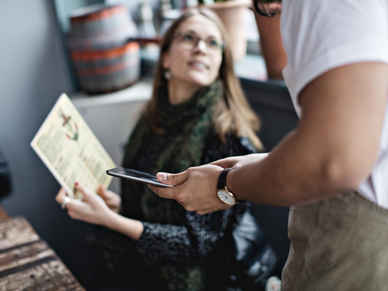 female customer asking from menu to waiter holding digital tablet at restaurant