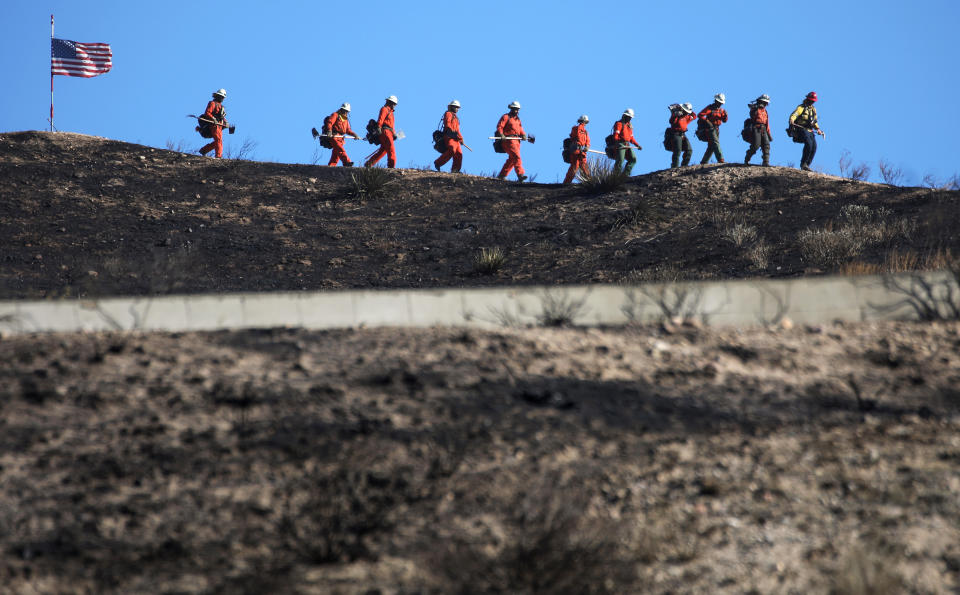 CANYON COUNTRY, CALIFORNIA - OCTOBER 25: Inmate firefighters march past an American flag, while led by a fire captain, as they work to put out hot spots from the Tick Fire on October 25, 2019 in Canyon Country, California. The fire has blackened 4,300 acres thus far with around 40,000 people under mandatory evacuation orders.  The inmates are from one of the 44 state prison fire camps, where inmates perform firefighting duties during the wildland fire season, for credit for early release and minimal pay.   (Photo by Mario Tama/Getty Images)