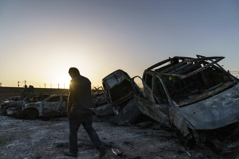 A worker passes torched cars piled up in a lot from clashes between Arabs, police and Jews in the mixed Arab-Jewish town of Lod, central Israel, Tuesday, May 25, 2021. Israel and Hamas reached a cease-fire weeks ago to bring 11 days of fighting in the Gaza Strip to an end. But the root causes of the cataclysmic upheavals that wracked Israel's mixed Jewish-Arab cities during that war have gone unaddressed. (AP Photo/David Goldman)