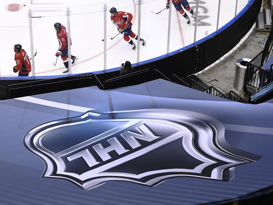 FILE - In this Aug. 14, 2020, file photo, an NHL logo is displayed as Washington Capitals players skate prior to NHL Eastern Conference Stanley Cup playoff hockey game against the New York Islanders in Toronto. The NHL plans to punish unvaccinated players more harshly if they test positive for the coronavirus as part of protocols for the upcoming season. Teams will be able to suspend unvaccinated players without pay if they cannot participate in hockey activities. Those who are fully vaccinated will have any COVID-19 positives treated as hockey injuries and still be paid. (Nathan Denette/The Canadian Press via AP)