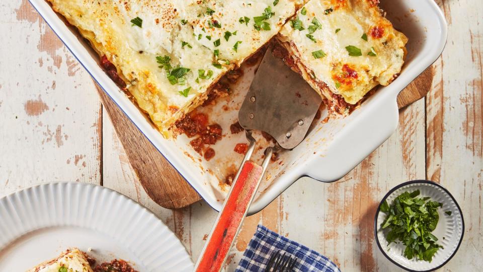 lasagna bolognese in a white rectangle baking dish with a spatula for serving