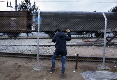 A stranded Syrian refugee watches a train speed past from behind a fence at the Greek-Macedonian border February 26, 2016, as he and his family wait for the border crossing to reopen near the Greek village of Idomeni. REUTERS/Yannis Behrakis