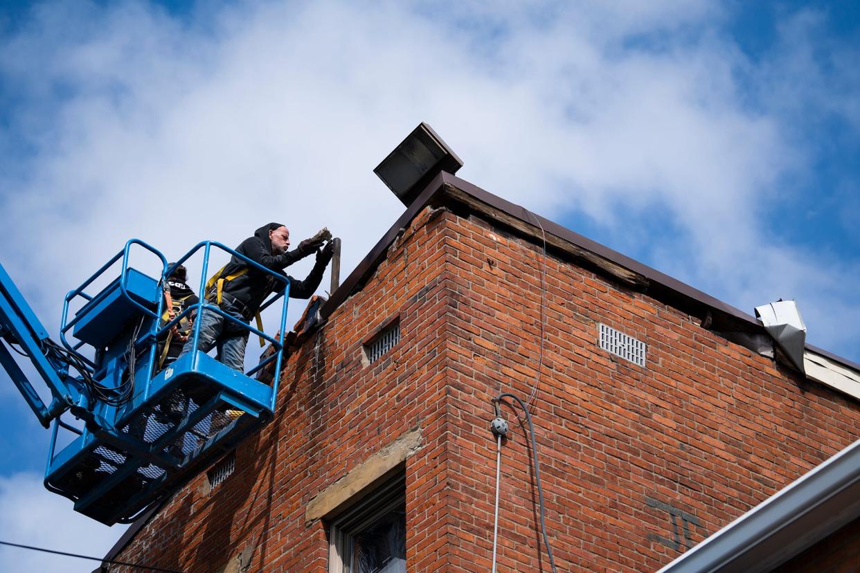 Workers remove loose bricks Monday after high winds last weekend brought down a section of a building's chimney and separated part of the roof from the commercial-residential building at Oak Street and Parks Avenue. The building was temporarily evacuated due to the damage, but residents and business owners were allowed to return after stabilization work was performed.