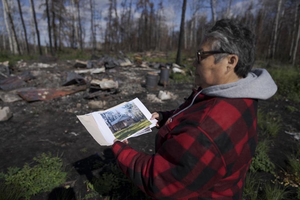 Julia Cardinal, right, shows a photo of what her cabin looked like before it was destroyed by wildfires, near Fort Chipewyan, Canada, on Sunday, Sep. 3, 2023. Cardinal lost the riverside cabin that was many things to her: retirement project, gift from from her husband, and somewhere to live by nature, as her family had done for generations. (AP Photo/Victor R. Caivano)