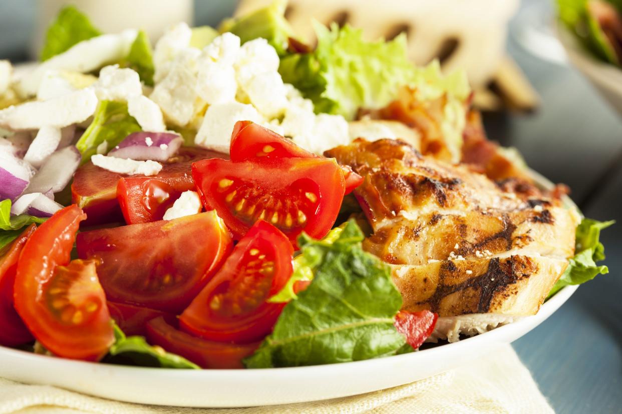 Closeup of chicken cobb salad on a white plate on a cloth napkin with a blurred background of ingredients