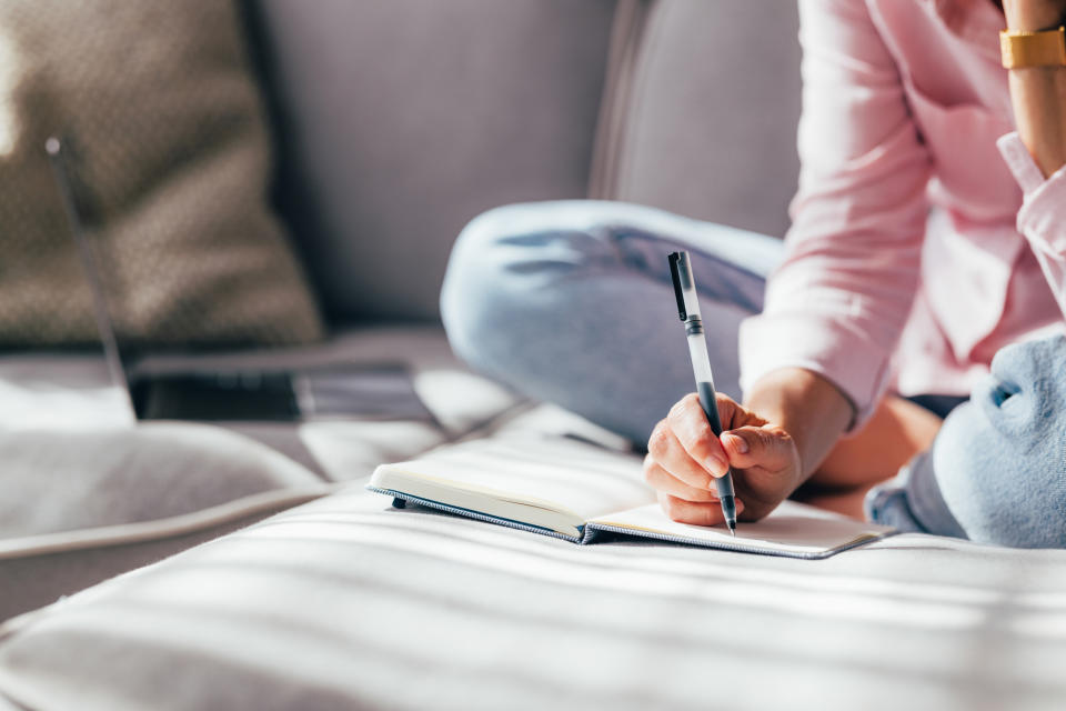 Person sitting on a couch, writing in a notebook, legs crossed. The image is related to an article categorized under Sex & Love