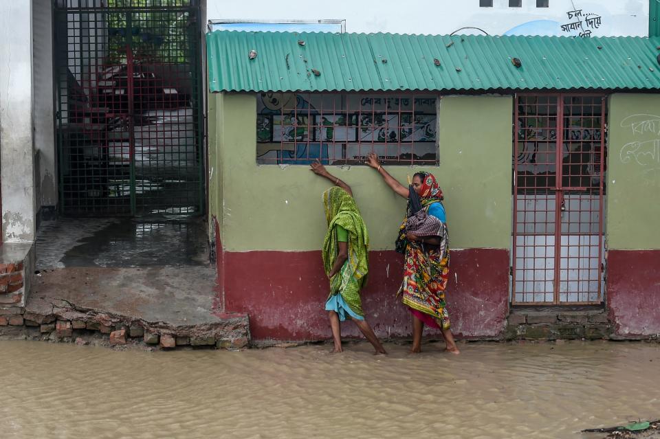 Residents walk along a house on a flooded street heading to a shelter ahead of the expected landfall of cyclone Amphan, in Dacope of Khulna district on May 20, 2020. - Several million people were taking shelter and praying for the best on Wednesday as the Bay of Bengal's fiercest cyclone in decades roared towards Bangladesh and eastern India, with forecasts of a potentially devastating and deadly storm surge. Authorities have scrambled to evacuate low lying areas in the path of Amphan, which is only the second "super cyclone" to form in the northeastern Indian Ocean since records began. (Photo by Munir uz Zaman / AFP) (Photo by MUNIR UZ ZAMAN/AFP via Getty Images)