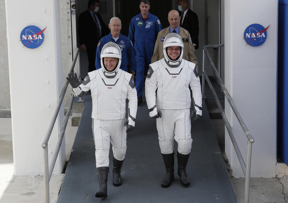 NASA astronauts Douglas Hurley, left, and Robert Behnken wave as they walk out of the Neil A. Armstrong Operations and Checkout Building on their way to Pad 39-A, at the Kennedy Space Center in Cape Canaveral, Fla., Wednesday, May 27, 2020. The two astronauts will fly on a SpaceX test flight to the International Space Station. For the first time in nearly a decade, astronauts will blast into orbit aboard an American rocket from American soil, a first for a private company. (AP Photo/John Raoux)