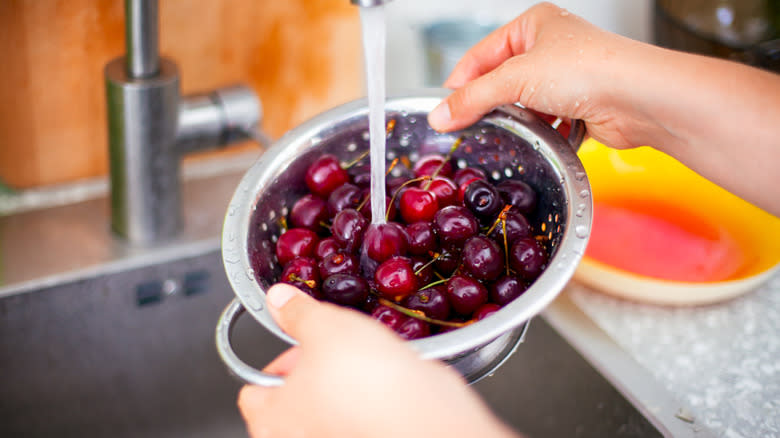 person washing cherries in colander