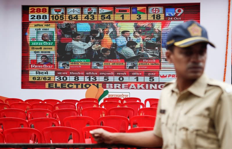 A policeman stands in front of a screen displaying Maharashtra state election results in Mumbai