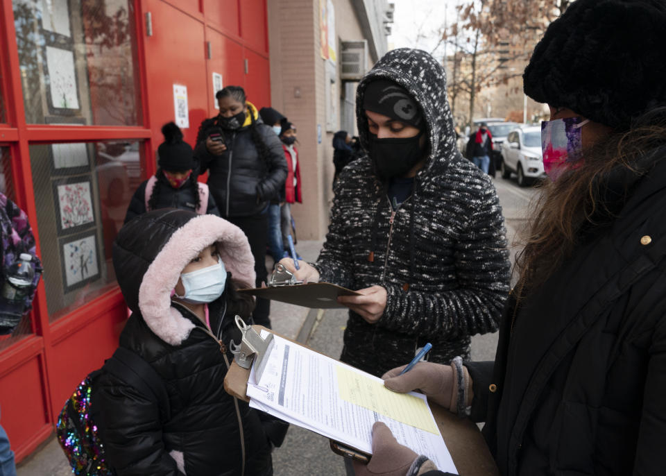 A parent, center, completes a form granting permission for random COVID-19 testing for students as he arrives with his daughter, left, at P.S. 134 Henrietta Szold Elementary School, Monday, Dec. 7, 2020, in New York. Public schools reopened for in-school learning Monday after being closed since mid-November. (AP Photo/Mark Lennihan)