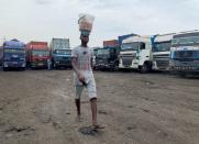 An egg-seller walks past food supply trucks parked at a garage in Lagos