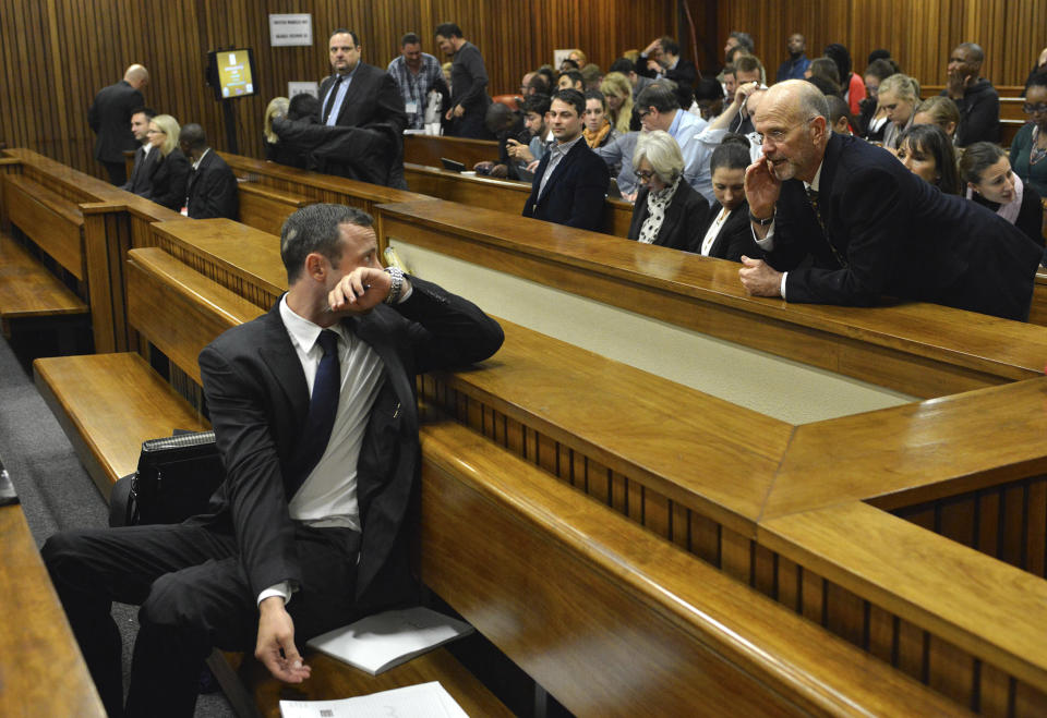 Oscar Pistorius, left, in the dock turns to his uncle Arnold Pistorius, back standing, on the second day of his trial at the high court in Pretoria, South Africa, Tuesday, March 4, 2014. Pistorius is charged with murder for the shooting death of his girlfriend, Reeva Steenkamp, on Valentines Day in 2013. (AP Photo/Antoine De Ras, Pool)