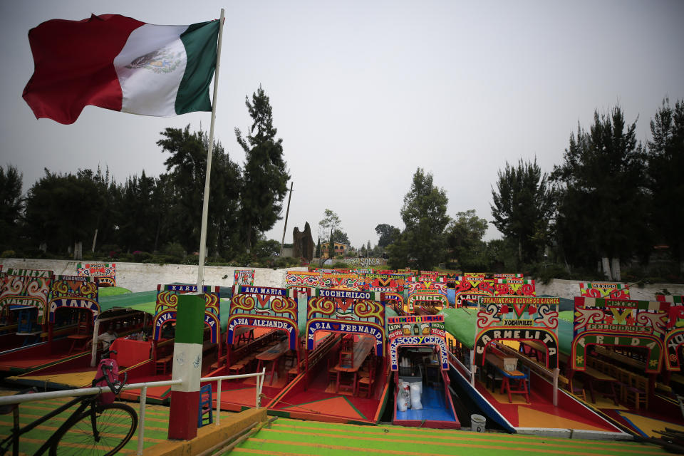 A Mexican flag flies over dozens of parked trajineras, the colorful passenger boats typically rented by tourists, families, and groups of young people, in Xochimilco, Mexico City, Friday, Sept. 6, 2019. The usually festive Nativitas pier was subdued and largely empty Friday afternoon, with some boat operators and vendors estimating that business was down by 80% on the first weekend following the drowning death of a youth that was captured on cellphone video and seen widely in Mexico. Borough officials stood on the pier to inform visitors of new regulations that went into effect Friday limiting the consumption of alcohol, prohibiting the use of speakers and instructing visitors to remain seated.(AP Photo/Rebecca Blackwell)