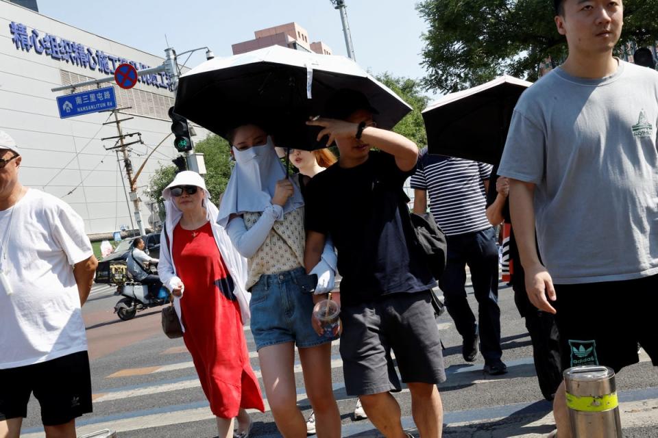 People shield themselves with umbrellas and face masks from the sun amid an orange alert for heatwave in Beijing (REUTERS)