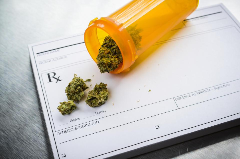 A tipped-over prescription bottle containing dried cannabis buds that's lying atop a doctor's prescription pad.