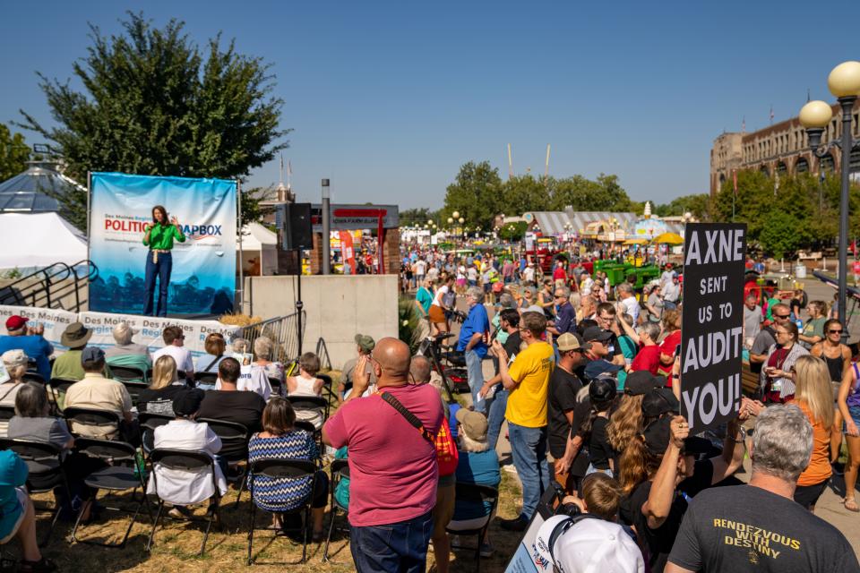 A protester holds a sign as Cindy Axne (D-IA) speaks at the Des Moines Register Political Soapbox during the Iowa State Fair, Wednesday, Aug. 17, 2022.