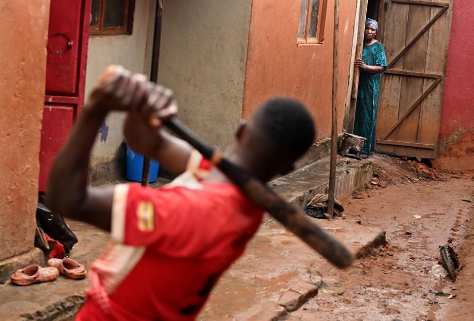 Dennis Kasumba practices his swing as his grandmother Edith Natenza watches outside there home.