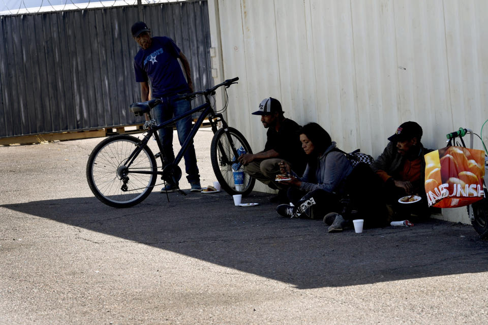 Homeless people sit in the shade of a box container while eating food from a soup kitchen, Thursday, May 30, 2024 in Phoenix. Sizzling sidewalks and unshaded playgrounds increasingly are posing risks for surface burns as air temperatures reach new highs during the searing summers in Southwest cities like Phoenix and Las Vegas. Very young children and older adults are especially at risk for contact burns. So are homeless people. (AP Photo/Matt York)