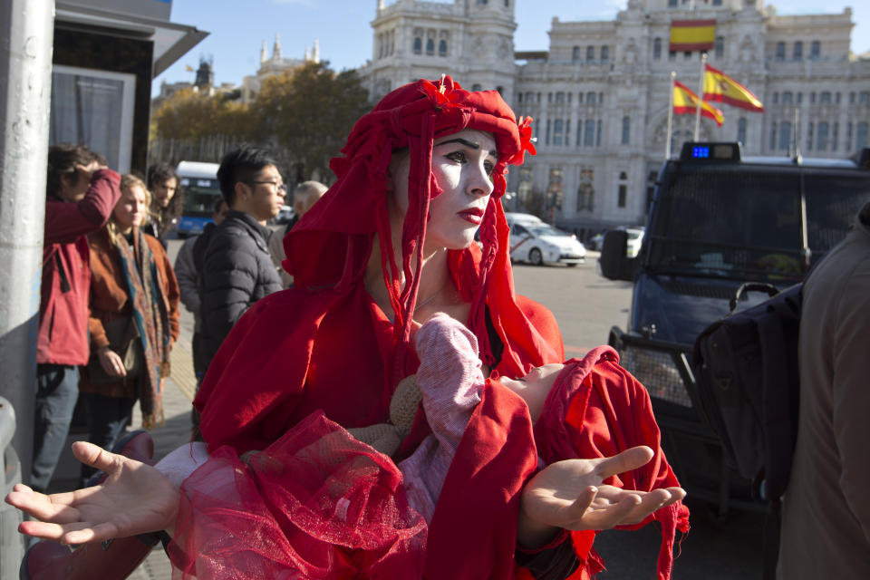 An activist takes part in a protest at the Cibeles fountain during a protest performance in Madrid, Spain, Tuesday, Dec. 3, 2019. Some 20 activists from the international group called Extinction Rebellion cut off traffic in central Madrid and staged a brief theatrical performance to protest the climate crisis. The activists held up a banner in Russian that read "Climate Crisis. To speak the truth. To take action immediately." Some 10 others dressed in red robes and with their faces whitened to symbolize the human species' peril danced briefly before police moved in to end the protest. (AP Photo/Paul White)