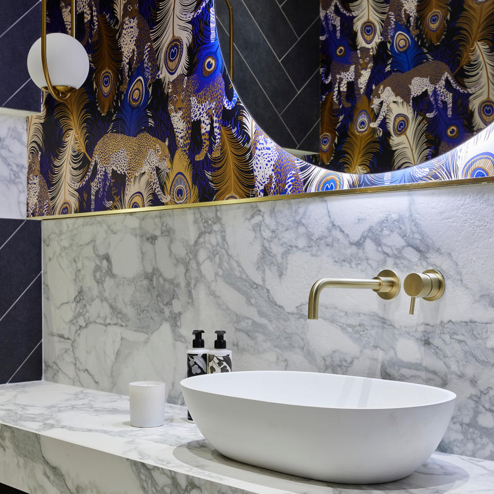 blue and marble cloakroom with cheetah peacock wallpaper, brass taps, blue tiles, marble splashback and counter top