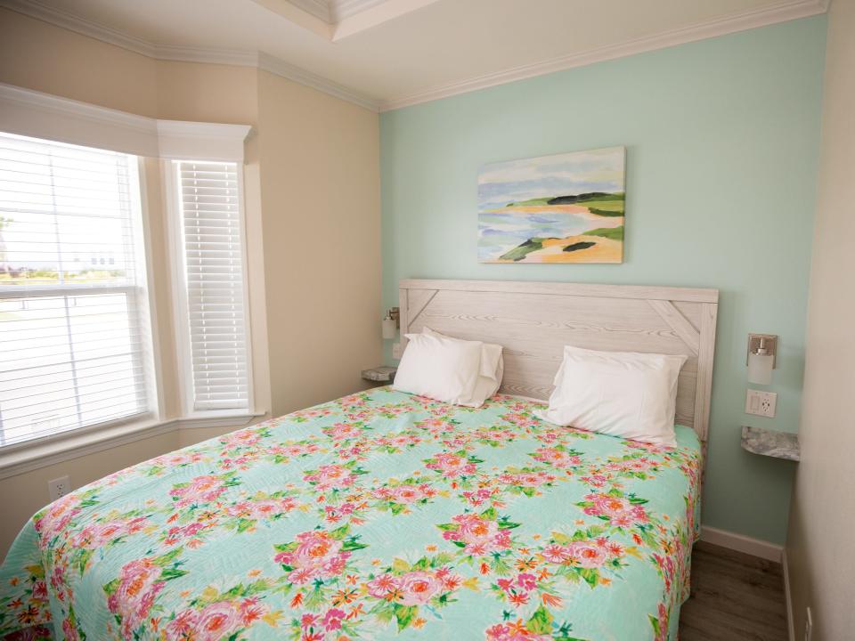 A bed with a flower pattern on the blanket. There's a picture on the wall.