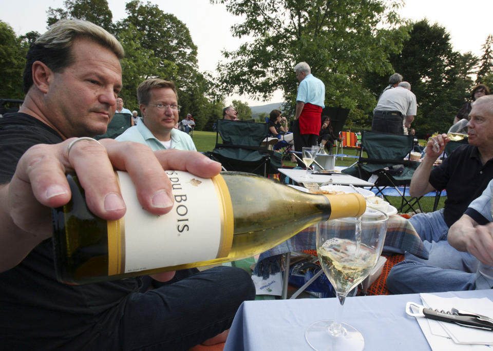 ARCHIVO – En esta fotografía del 7 de julio de 2006 Michael Van Parks, izquierda, sirve vino con sus amigos Bill Beeman, centro, y Don Usher, derecha, todos de West Hartford, Connecticut, mientras tienen un picnic en Tanglewood en Lenox, Massachussetts antes de la noche inaugural de la Orquesta Sinfónica de Boston. La Orquesta Sinfónica de Boston anunció el 19 de marzo de 2021 que su temporada al aire libre en Tanglewood regresará con conciertos en vivo y en persona del 9 de julio al 16 de agosto. El festival se canceló en 2020 por la pandemia de COVID-19. (Foto AP/Michael Dwyer, archivo)