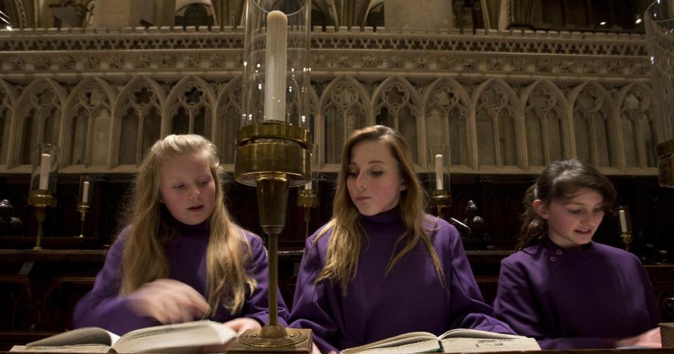 In this Wednesday, Jan. 22, 2014 photo, Choristers Chloe Chawner, right, Poppy Braddy, centre, and Abby Cox look at their him books Canterbury Cathedral, Canterbury, England, as the first all female choir at the cathedral rehearses prior to their debut on Jan. 25. The pure, high voices of the choir soar toward the vaulted ceiling of Canterbury Cathedral as they have for more than 1,000 years. Just one thing is different - these young choristers in their purple cassocks are girls, and their public debut at Evensong on Saturday will end centuries of all-male tradition.Canterbury is not the first British cathedral to set up a girls' choir, but as mother church of the 80 million-strong Anglican Communion - one struggling with the role of women in its ranks - its move has special resonance.(AP Photo/Alastair Grant)