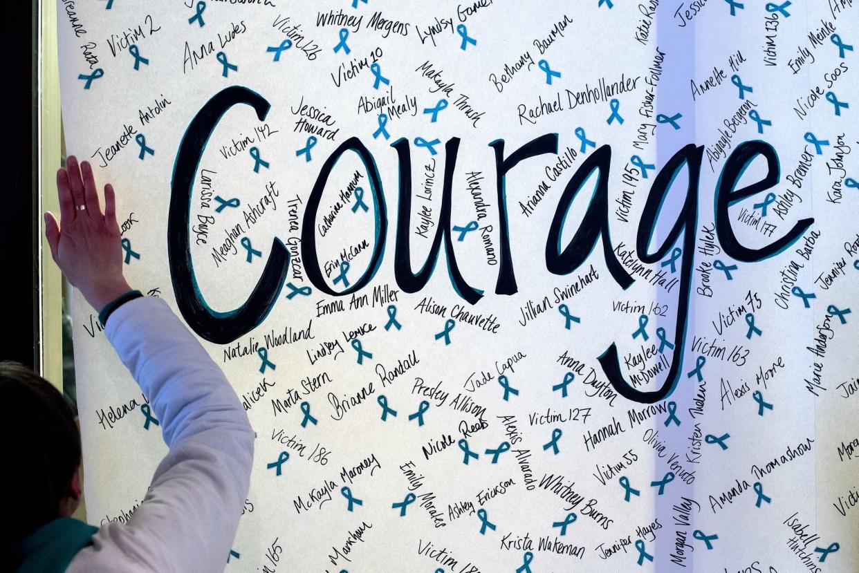 A ReclaimMSU volunteer helps put up a sign reading 'courage' with the names of Nassar survivors during the "One Year On: Celebrating Courage and Creating Change" event. 
Nick King/Lansing State Journal
A ReclaimMSU volunteer helps put up a sign reading 'courage' with the names of Nassar survivors during the "One Year On: Celebrating Courage and Creating Change" event on Thursday, Jan. 24, 2019, outside the Hannah Administration Building on the Michigan State University campus in East Lansing. The event was organized by Reclaim MSU and held on the one-year anniversary of Larry Nassar's sentencing.