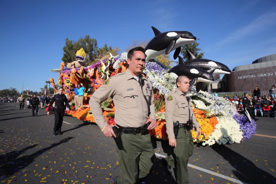 Police officers walk with the SeaWorld Parks and Entertainment float moving along Colorado Boulevard during the Tournament of Rose Parade in Pasadena, Calif., Wednesday, Jan. 1, 2014. (AP Photo/Ringo H.W. Chiu)