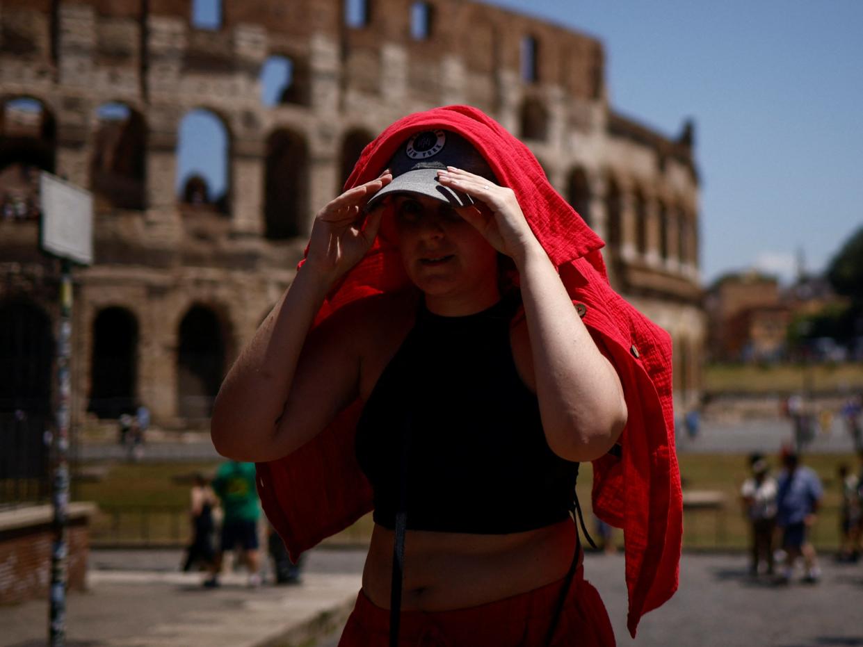 A woman shelters from the sun with a shirt near the Colosseum during a heatwave across Italy (REUTERS)