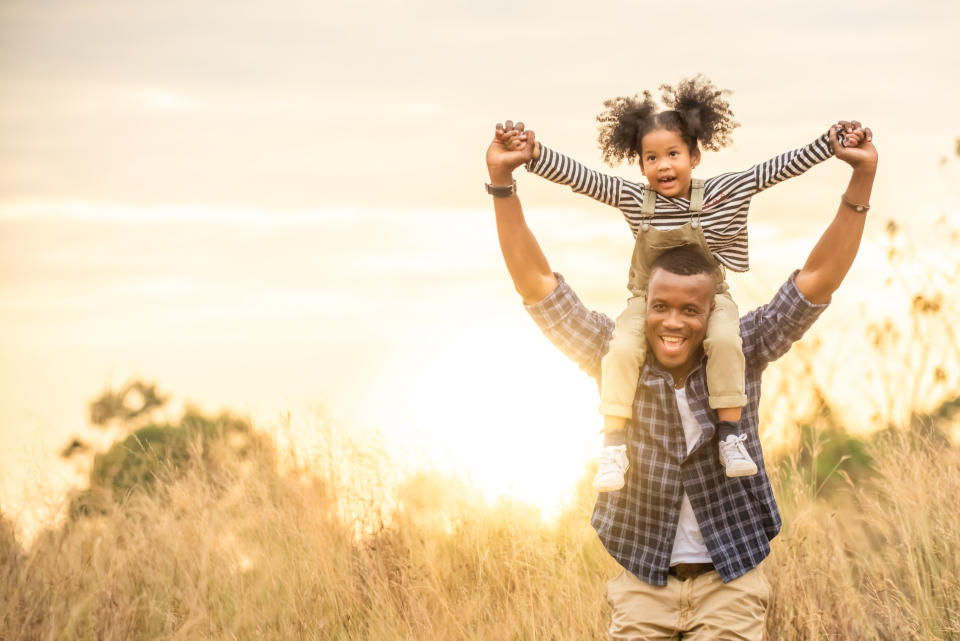 African daughter sitting on her father neck while hiking on the mountain