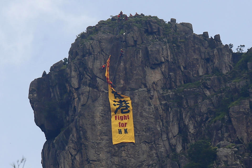 Firefighters remove a yellow banner with the words "Fight for Hong Kong" in Chinese and English which is hung on the Lion Rock mountain by pro-democracy protesters in Hong Kong, Sunday, June 16, 2019. Hong Kong was bracing Sunday for another massive protest over an unpopular extradition bill that has highlighted the territory's apprehension about relations with mainland China, a week after the crisis brought as many as 1 million into the streets. (AP Photo/Kin Cheung)