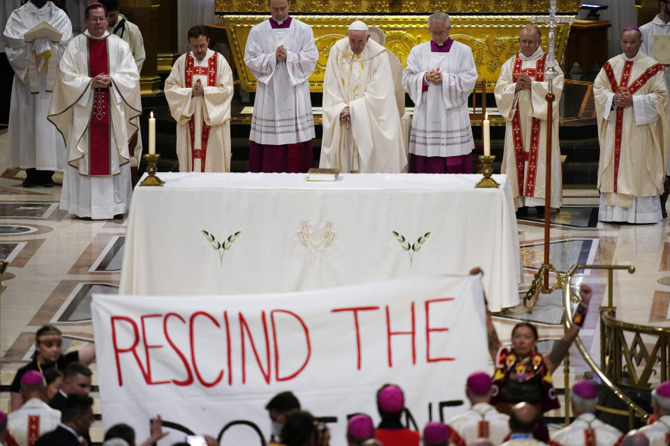 Protesters hold up a banner during a mass with Pope Francis, center top, at the National Shrine of Saint Anne de Beaupre, Thursday, July 28, 2022, in Saint Anne de Beaupre, Quebec. Pope Francis is on a "penitential" six-day visit to Canada to beg forgiveness from survivors of the country's residential schools, where Catholic missionaries contributed to the "cultural genocide" of generations of Indigenous children by trying to stamp out their languages, cultures and traditions. (AP Photo/John Locher)