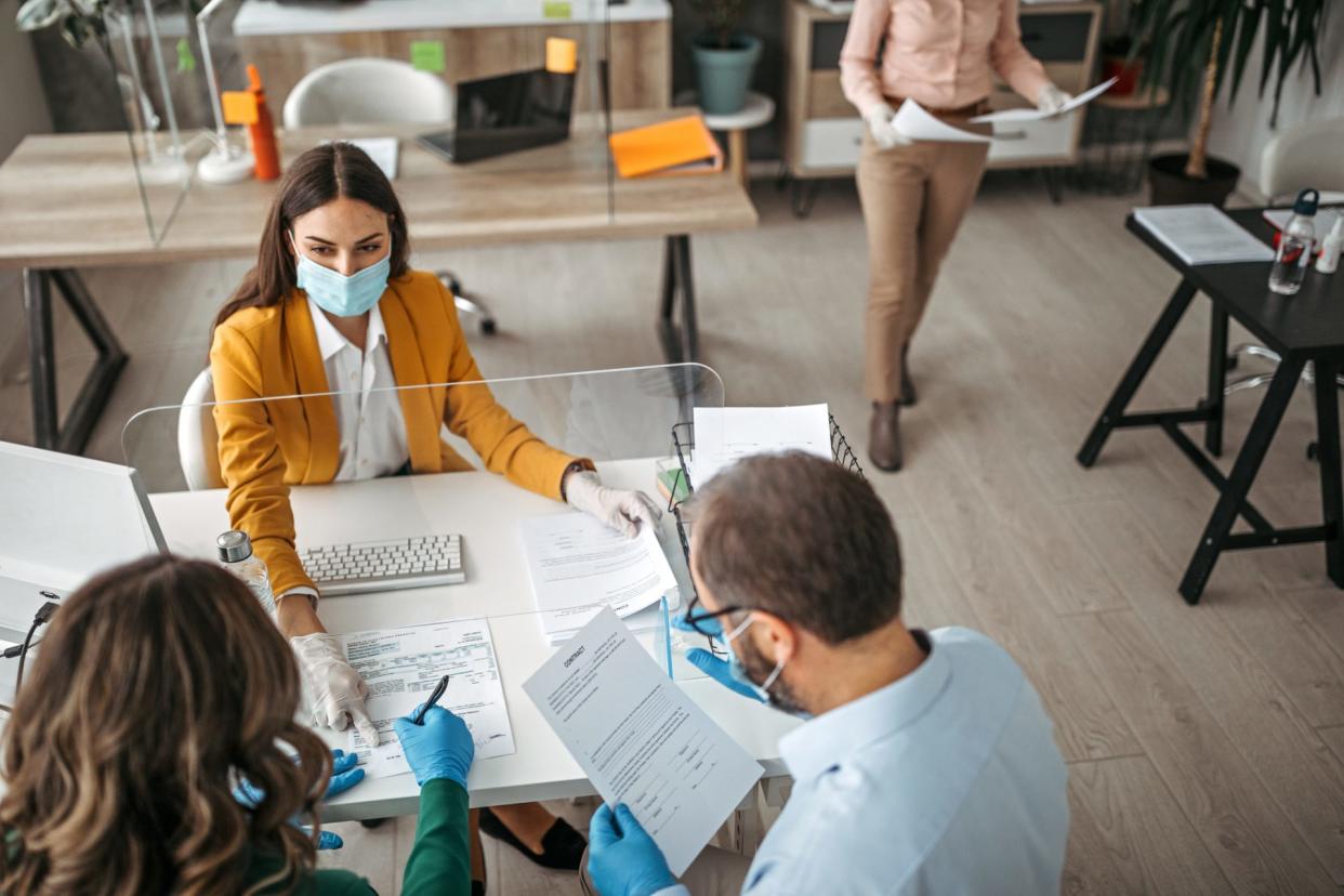 Couple signing a document on a meeting at insurance agent office wearing protective gloves and face mask.