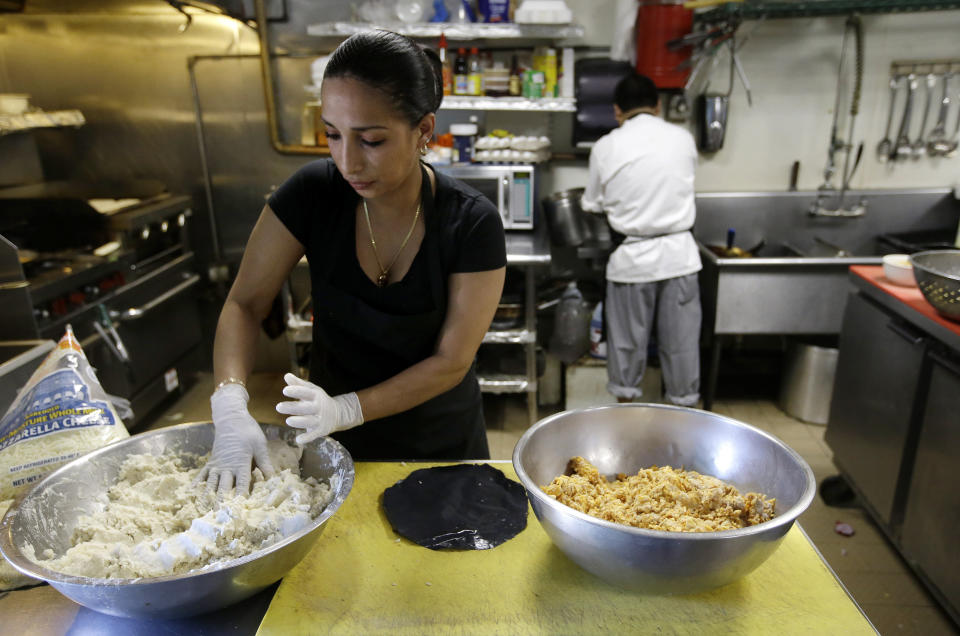 In this Thursday, June 27, 2019 photo Mariana Moncada, left, originally of Honduras, prepares food in a kitchen, in Chelsea, Mass. A recent study by the Pew Research Center shows the number of Central Americans in the United States increased over the last decade. Chelsea has exemplified that trend with a population that is more than 60 percent Latino. (AP Photo/Steven Senne)