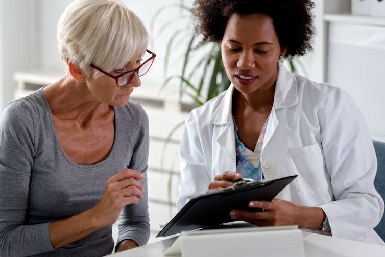 An older woman and her female doctor both look down at a clipboard the doctor is holding.