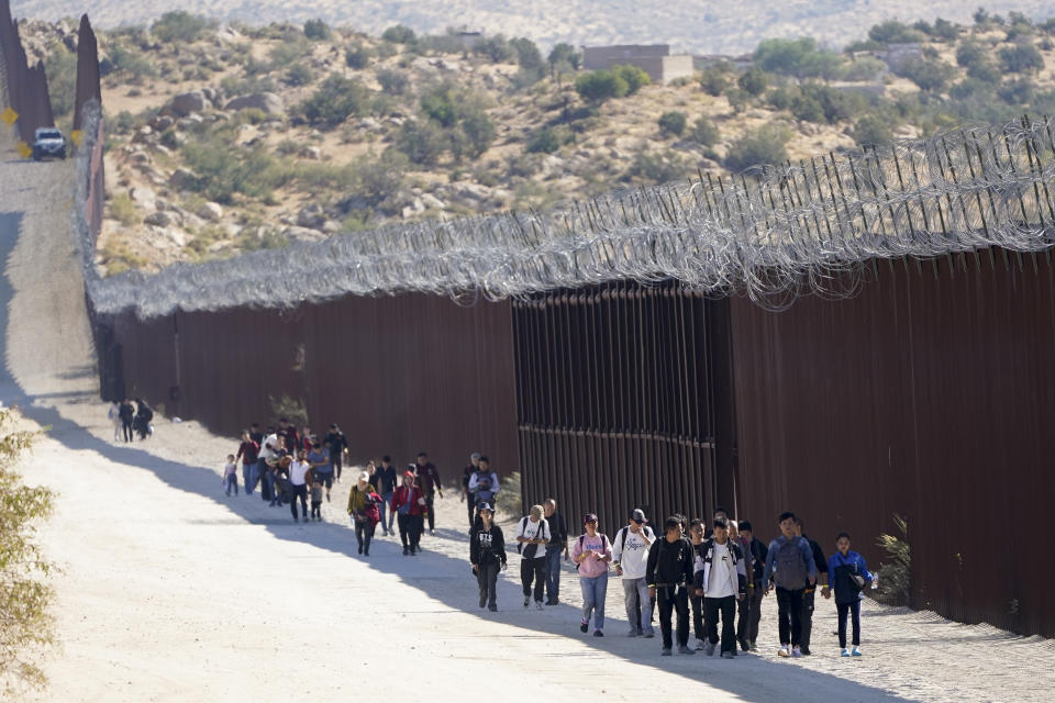 A group of people, including many from China, walk along the wall after crossing the border with Mexico to seek asylum, Tuesday, Oct. 24, 2023, near Jacumba, Calif. A major influx of Chinese migration to the United States on a relatively new and perilous route through Panama's Darién Gap jungle has become increasingly popular thanks to social media. (AP Photo/Gregory Bull)