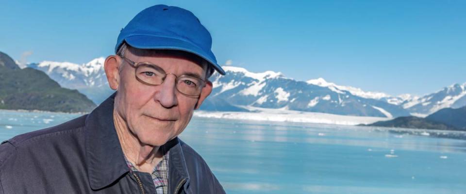 Portrait of senior man wearing blue cap with Hubbard glacier in background.