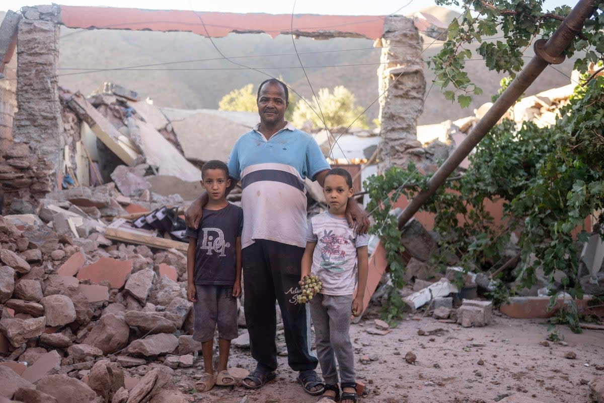 Mohammed Elhmatif and his sons, Rayan, right, and Ali, stand amid the rubble of their home in Ijjoukak village, near Marrakech (AP)
