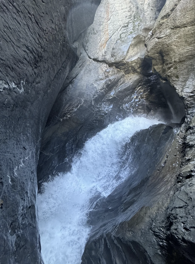 A mighty waterfall plunges between high, rugged rocks in a narrow gorge, creating mist and rushing water below