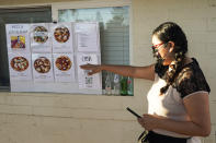 Ruby Salgado, points to the pizza menu posted outside her home at her family's makeshift pizza restaurant in Scottsdale, Ariz. on April 3, 2021. Beaten down by the pandemic, some laid-off or idle restaurant workers have pivoted to dishing out food from home. Salgado, 26, and her husband, Jose Hernandez, spend their weekends making pizzas in a backyard oven they built. Some nights, they churn out as many as 30 pies with toppings like fennel sausage, fresh mozzarella and carne asada. (AP Photo/Ross D. Franklin)