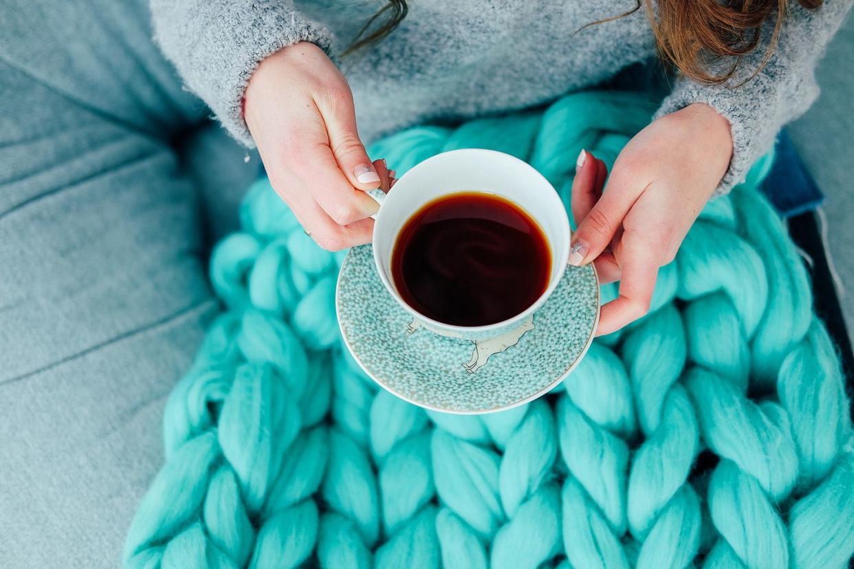 feminine hands holding cup of black tea over teal cozy knitted blanket