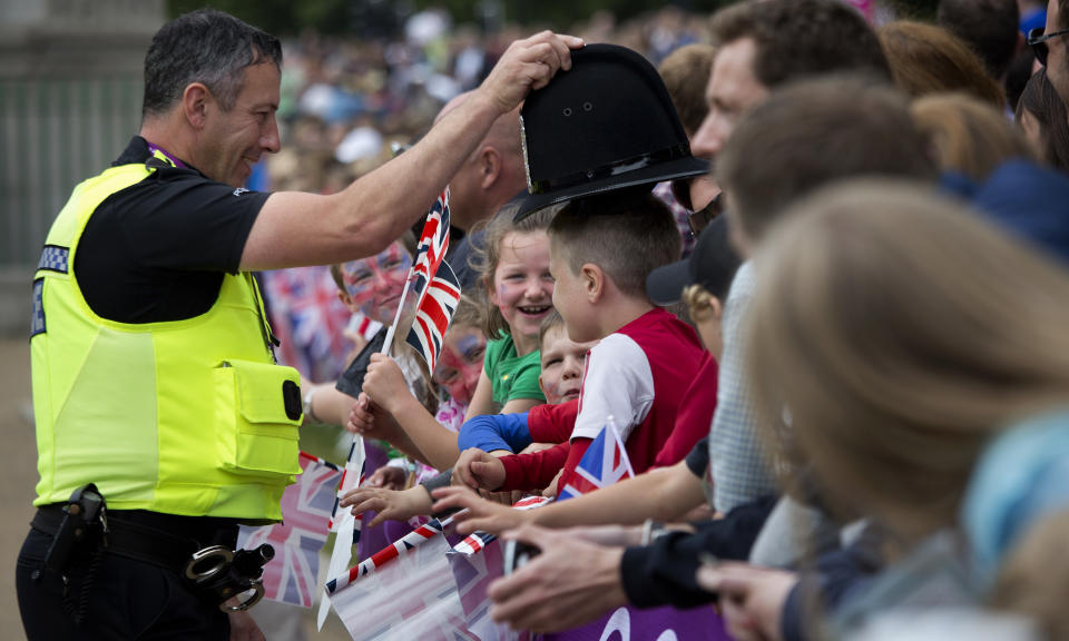 In this Tuesday, Aug. 7, 2012 photo, a policeman jokes with children as they wait for men's triathlon to pass by at the 2012 Summer Olympics, in London. (AP Photo/Emilio Morenatti)