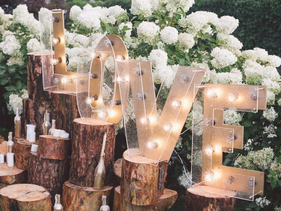 Lights in letters that spell out "Love"arranged on wooden logs in front of white flowers